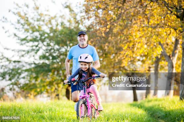 vader en dochter genietend van sport activiteit buitenshuis - familie fietsen close up stockfoto's en -beelden