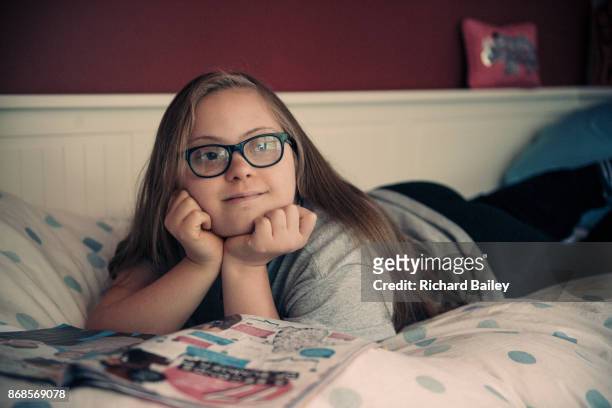 Teen girl who has Down syndrome, laying on her bed reading a magazine.