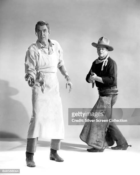 Portrait of American actors James Stewart and John Wayne as they pose in front of a white background in costume for 'The Man Who Shot Liberty...