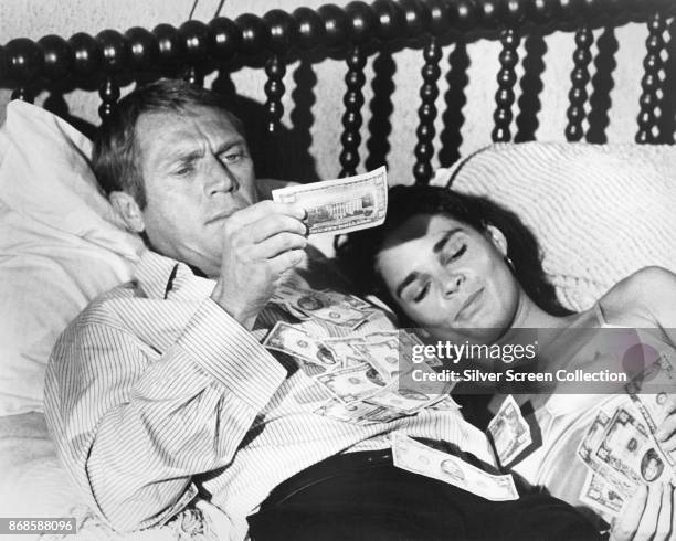 American actors Steve McQueen and Ali MacGraw lie in bed covered by money in a scene from the film 'The Getaway' , 1972.