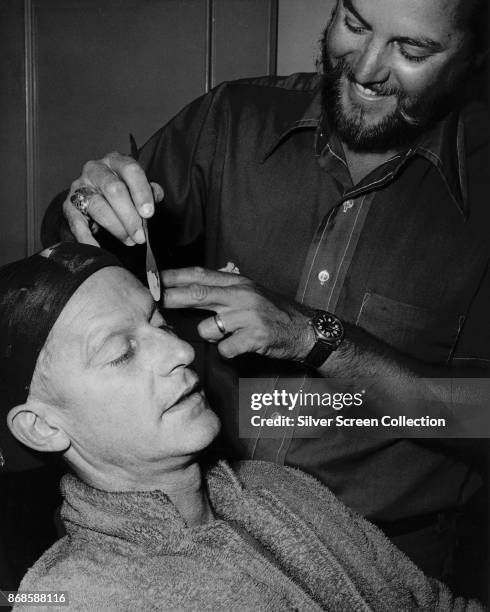 Portrait of American makeup artist Fred Blau works on English-American actor Roddy McDowall to transform him into character backstage for an episode...