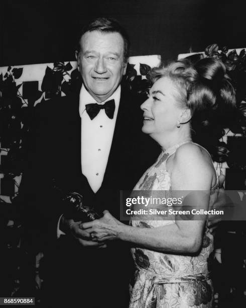 American actors John Wayne and Joan Crawford hold a trophy at 27th Annual Golden Globe Awards ceremony at the Cocoanut Grove, Los Angeles,...
