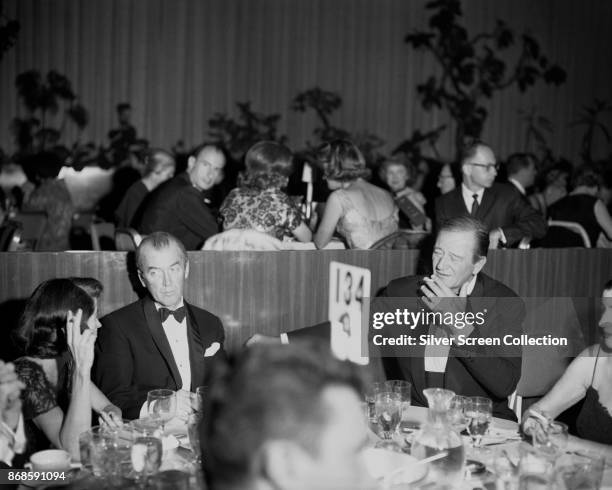 American actors James Stewart and John Wayne sit with unidentified others during a dinner event, 1960s.