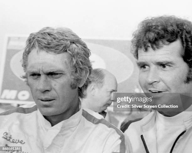 American actor Steve McQueen , in a personalized racing suit, poses with an unidentified man as he promotes the film 'Le Mans' , France, 1971.