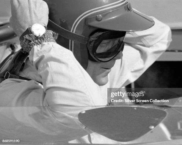 View of American actor Steve McQueen , in Firestone racing suit, adjusts his goggles as he sits in a car at Riverside Raceway, Riverside, California,...