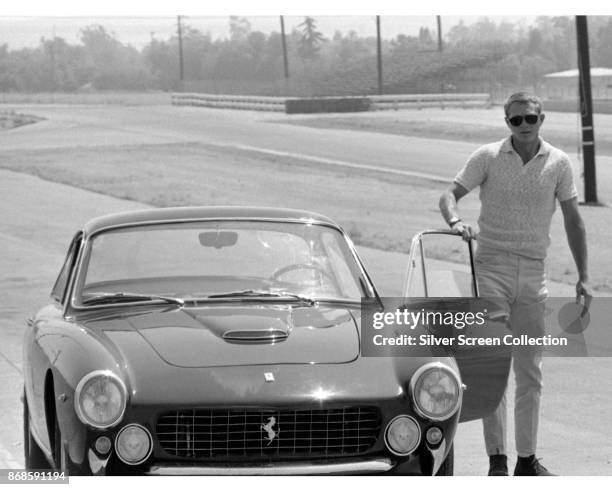 View of American actor Steve McQueen as he stands beside the open door of a Ferrari Lusso 250 Berlinetta, late 1960s.