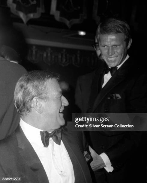 View of American actors John Wayne and Steve McQueen as they greet one another at an unspecified event, 1960s or 1970s.