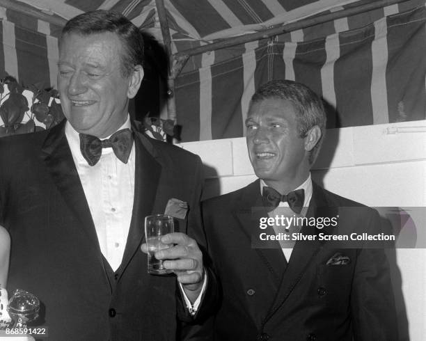 American actors John Wayne and Steve McQueen share a laugh during the 24th Annual Golden Globe Awards ceremony at the Cocoanut Grove, Los Angeles,...