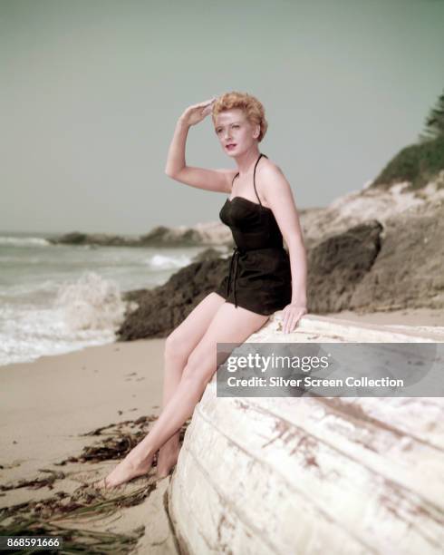 Portrait of Scottish actress Deborah Kerr , in a black swimsuit, as she leans against an overturned boat on a beach, 1940s or 1950s.