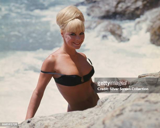 German actress and model Elke Sommer , in a black bikini top, on a rocky beach in a scene from 'Deadlier Than the Male' , 1967.