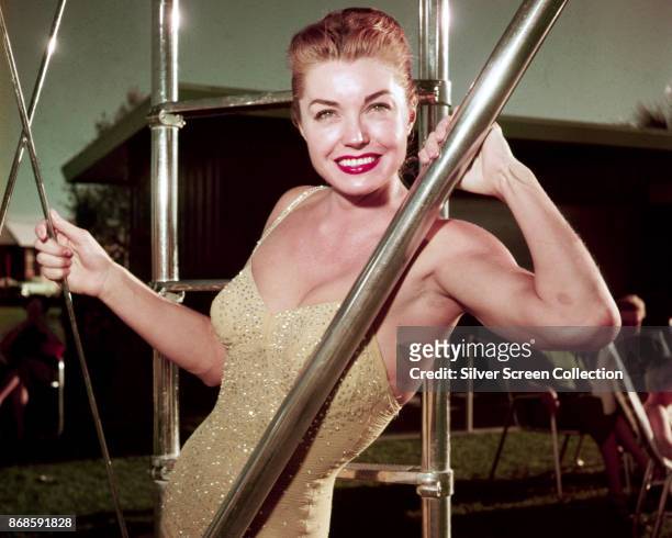 Portrait of American swimmer and actress Esther Williams , in a gold, sequin swimsuit, as she poses beside the ladder to a diving board, mid 1950s.