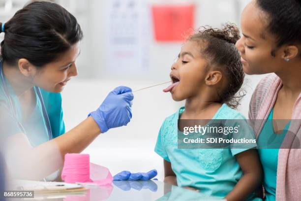 brave little girl opens wide for throat swab at doctor - tongue depressor stock pictures, royalty-free photos & images