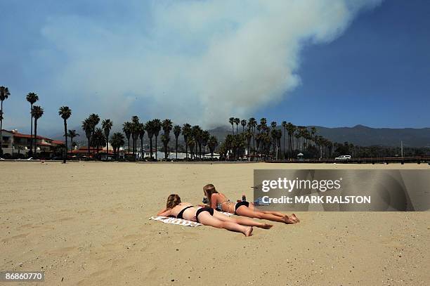 Two girls sunbathe on West Beach as a large smoke clouds billows behind during the Jesusita Fire in the hills of Santa Barbara, May 8, 2009....