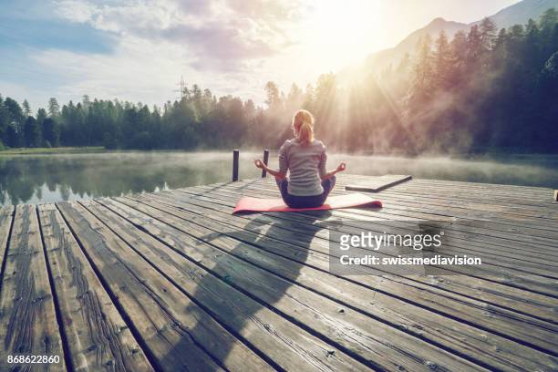 kaukasische mädchen ausübung yoga in der natur, morgen am see in der schweiz - yoga stock-fotos und bilder