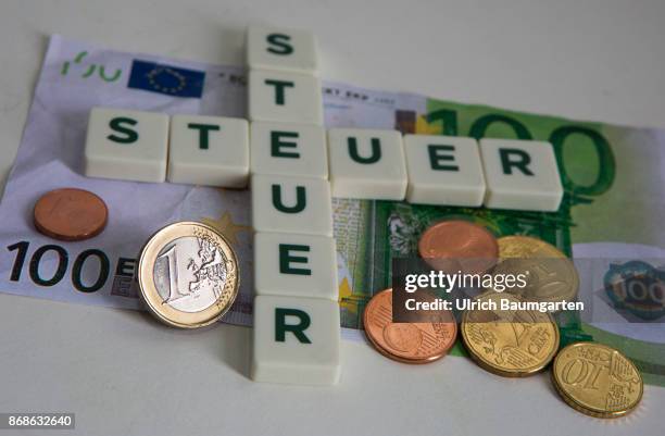 Symbol photo on the subject of taxes. The photo shows the words taxe, placed from scrabble stones, and different euro coins.