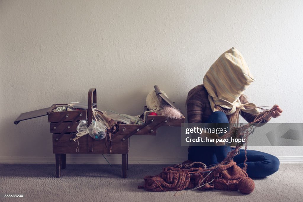 Woman with a bag on her head untangling yarn.