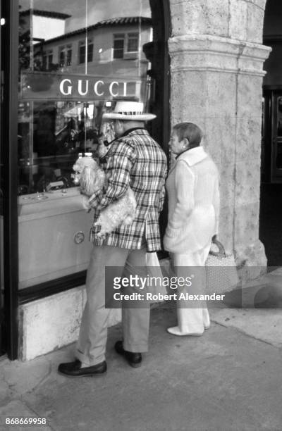 Couple with a poodle window shop in front of a Gucci store on Worth Avenue in Palm Beach, Florida, in 1982.
