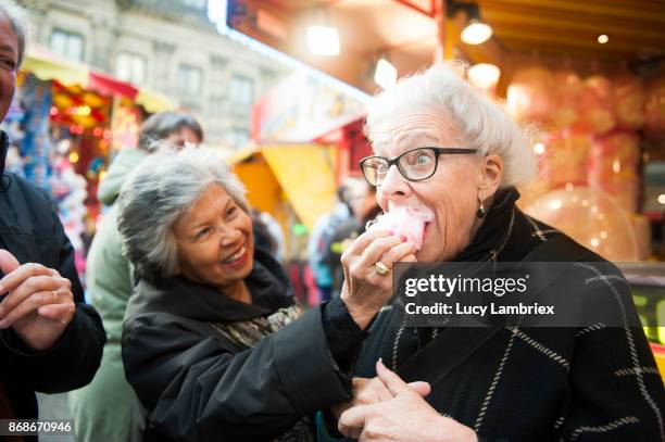 active senior girlfriends enjoying cotton candy at the fair in amsterdam - septuagénaire photos et images de collection
