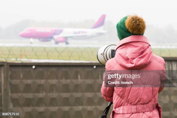 jeune femme avec super téléobjectif montre wizair avion sur la piste. - plane spotting photos et images de collection