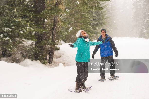 smiling ethnic senior couple snowshoeing in the forest - active seniors winter stock pictures, royalty-free photos & images