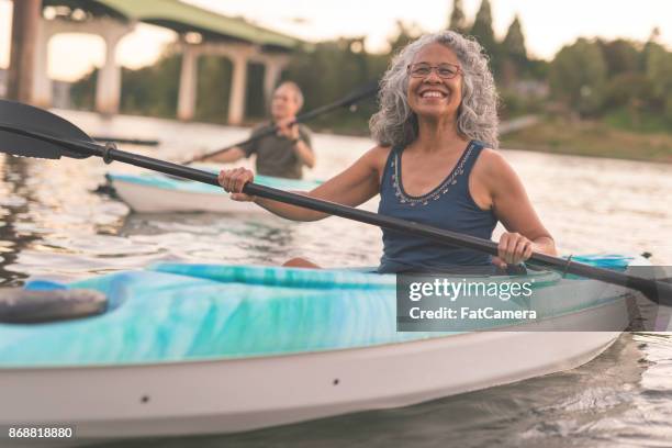 an ethnic senior woman smiles while kayaking with her husband - kayaker woman stock pictures, royalty-free photos & images