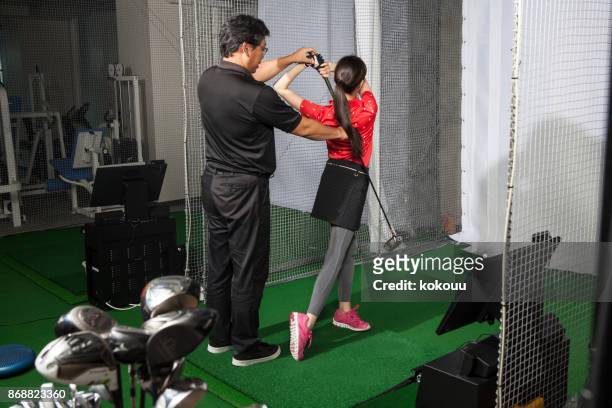 a woman practicing at a golf studio and a man with a coach. - indoor golf stock pictures, royalty-free photos & images
