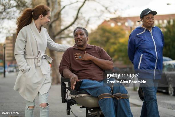 la ragazza adolescente bianca che parla con un uomo e una donna afroamericani disabili presieduti da ruote quando camminano per strada insieme - the bronx foto e immagini stock