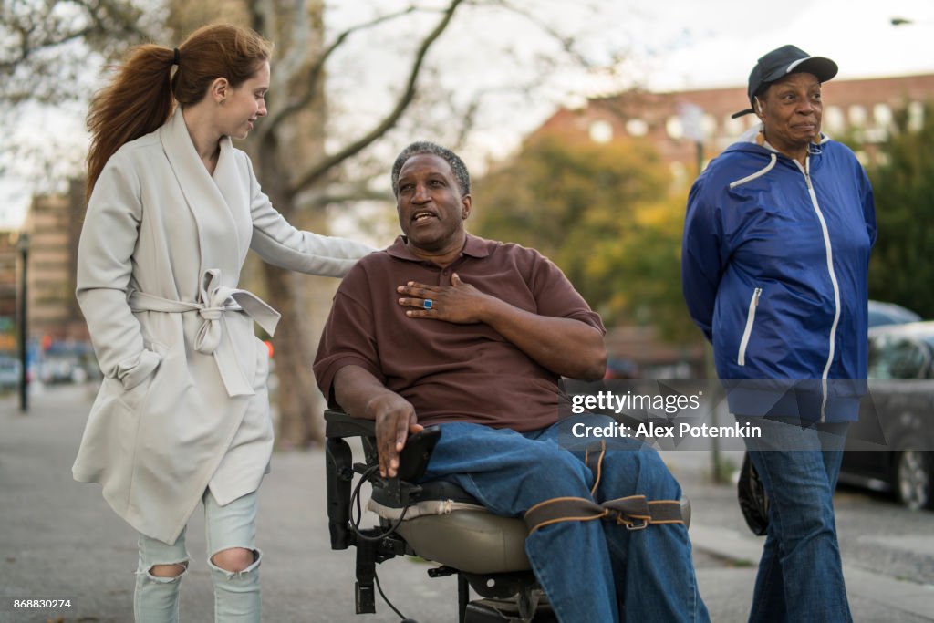 The White teenager girl talking with disabled wheel-chaired African American man and woman when they walking on the street together