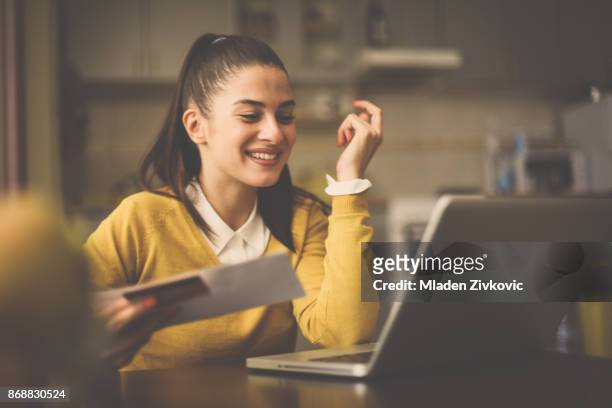 happy woman at home holding credit card and using laptop. - debit cards credit cards accepted stock pictures, royalty-free photos & images