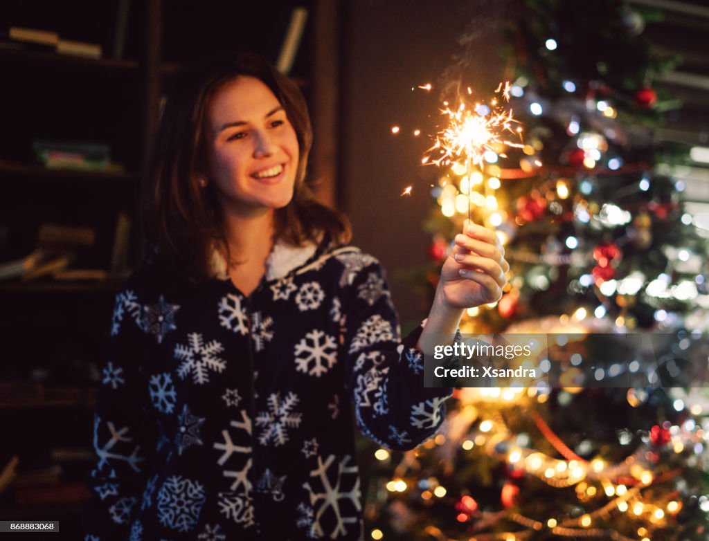 Woman holding sparkler in front of a Christmas tree