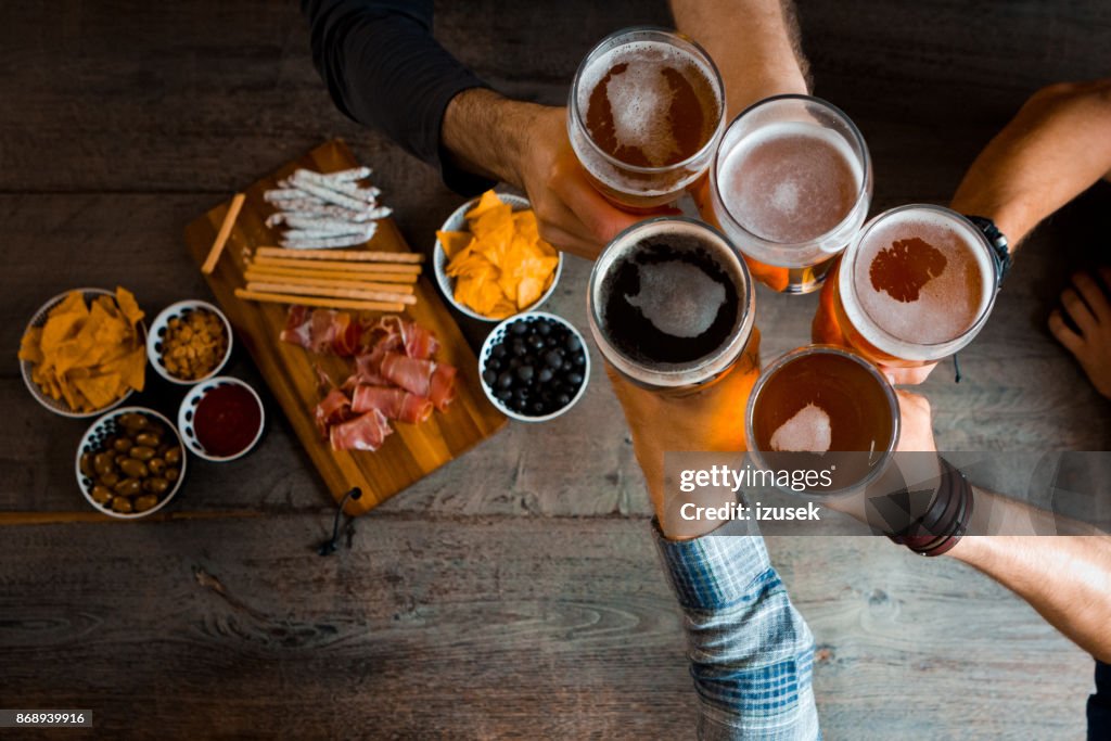 Top view of friends toasting with beer glasses in the pub