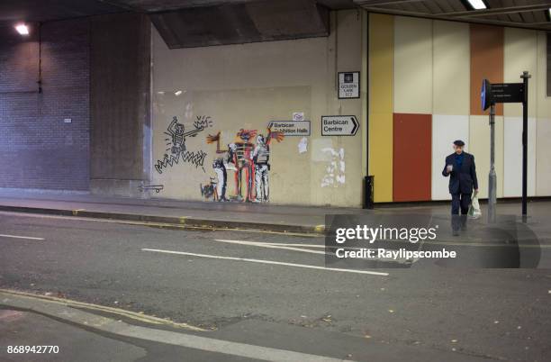 man walking past a banksy mural, near the barbican art centre in golden lane in london. - banksy artworks at barbican centre stock pictures, royalty-free photos & images