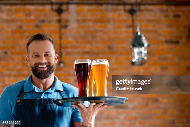 happy bartender holding serving tray with glasses of beer - hipster barkeeper stock pictures, royalty-free photos & images