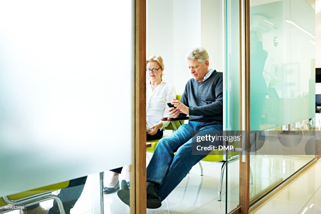 Senior man sitting in waiting room using mobile phone