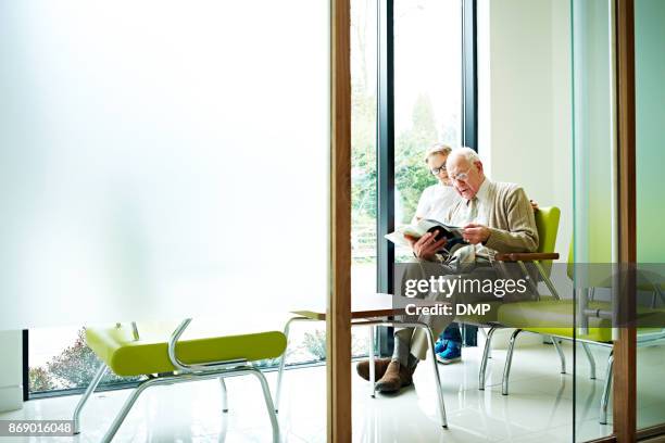 grandfather and grandson sitting in waiting room - doctor publication stock pictures, royalty-free photos & images