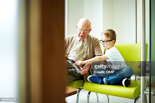 kleiner junge mit seinem großvater sitzen im wartezimmer - treats magazine stock-fotos und bilder