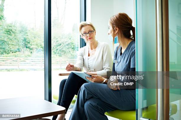 volwassen vrouwelijke patiënt praten met verpleegkundige in wachtkamer - patients in doctors waiting room stockfoto's en -beelden
