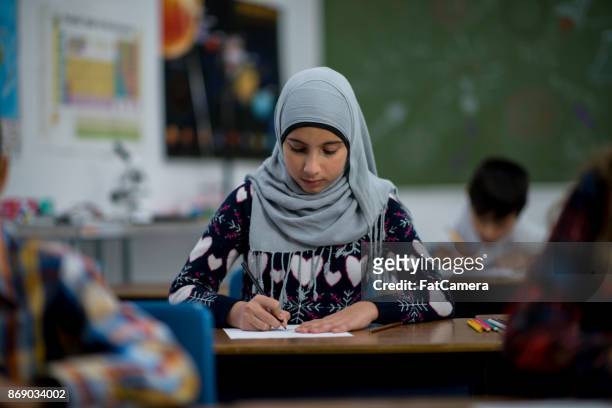 muslim girl doing a school assignment in a classroom - islamic school stock pictures, royalty-free photos & images