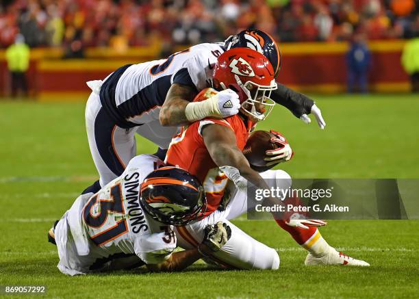 Defenders Von Miller and Justin Simmons of the Denver Broncos tackle running back Kareem Hunt of the Kansas City Chiefs during the first half on...