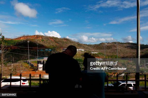 Couple watches from the school entrance to the mountains in Barranquitas, Puerto Rico October 31, 2017. Twenty people from Barranquitas have been...