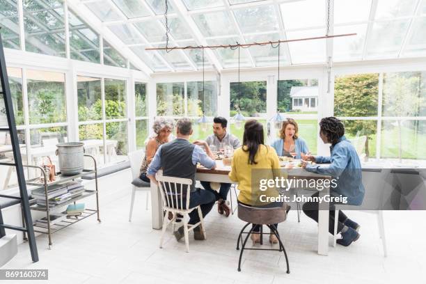 six amis assis autour de la table de dîner dans naturellement allumé conservatoire parler - conservatory house photos et images de collection