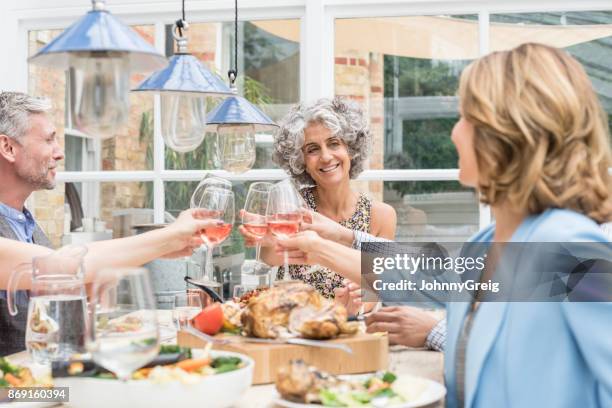 two mature women toasting wine glasses with man in his 50s at dinner table - rose wine stock pictures, royalty-free photos & images