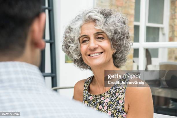 mature woman with grey curly hair and floral top smiling and talking to man - woman sitting top man stock pictures, royalty-free photos & images