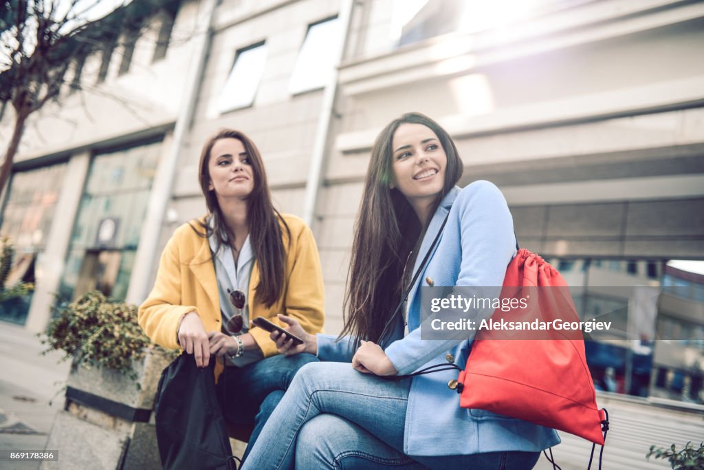 Two Smiling Females Waiting for Uber Taxi in the City Street