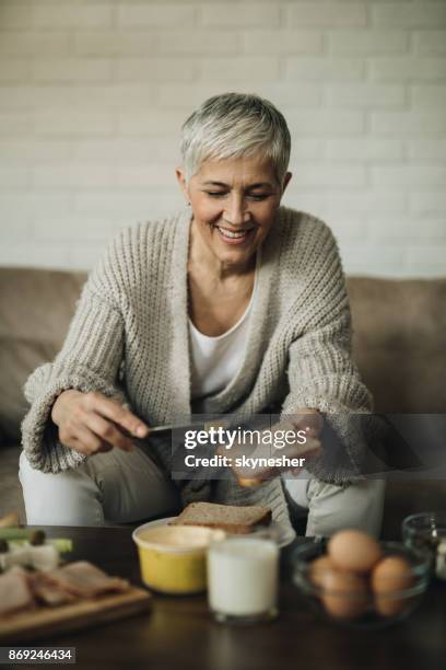 feliz mujer madura haciendo un sándwich para el desayuno. - untar de mantequilla fotografías e imágenes de stock