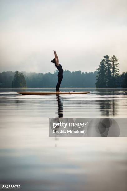 sup yoga - sun aanhef opwaartse salute - urdhva hastasana - practioners enjoy serenity of paddleboard yoga stockfoto's en -beelden