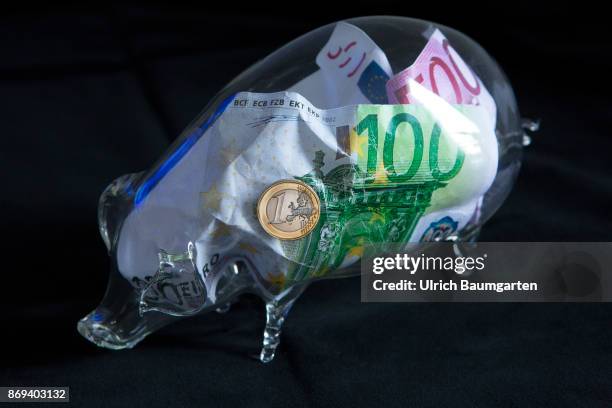 Symbol photo on the subject money save. The picture shows euro banknotes and a one euro coin in a glass piggy bank.