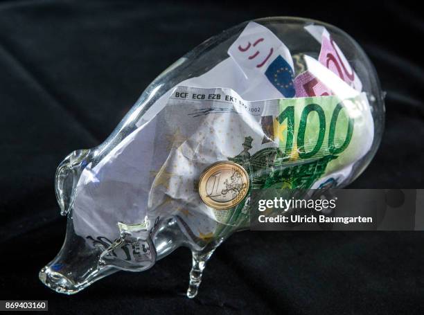 Symbol photo on the subject money save. The picture shows euro banknotes and a one euro coin in a glass piggy bank.