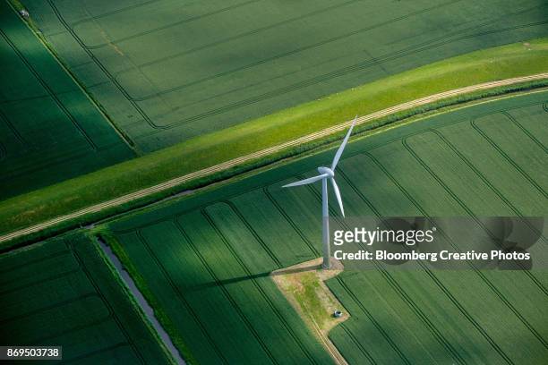 a wind turbine stands in a field of agricultural crops - umweltfreundliche energieerzeugung stock-fotos und bilder