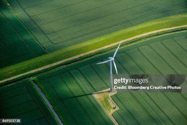 a wind turbine stands in a field of agricultural crops - aerogenerador fotografías e imágenes de stock